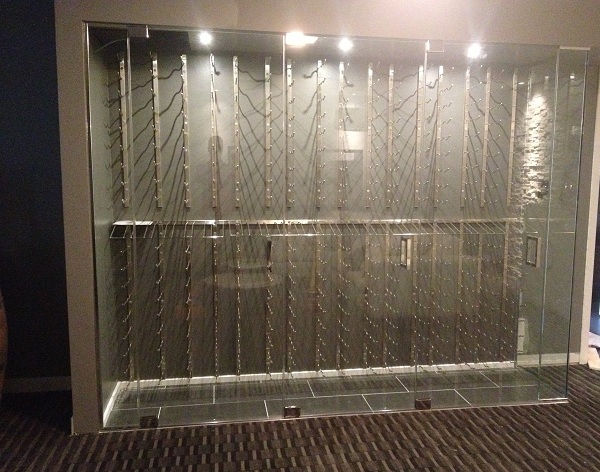 Cava de vino acristalada con soportes metálicos de pared para botellas e iluminación integrada.