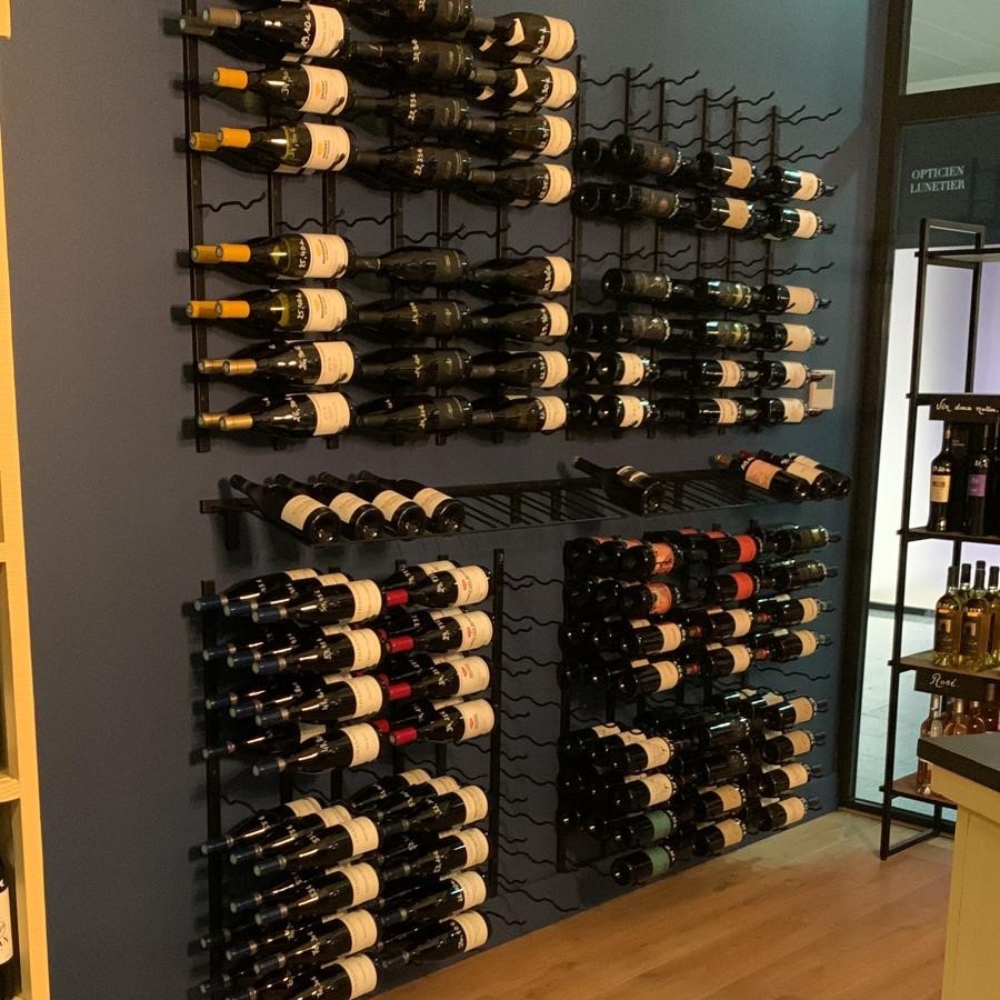 Muro de vino profesional con soportes negros de pared para presentar botellas en una tienda, cava, restaurante o espacio de degustación.