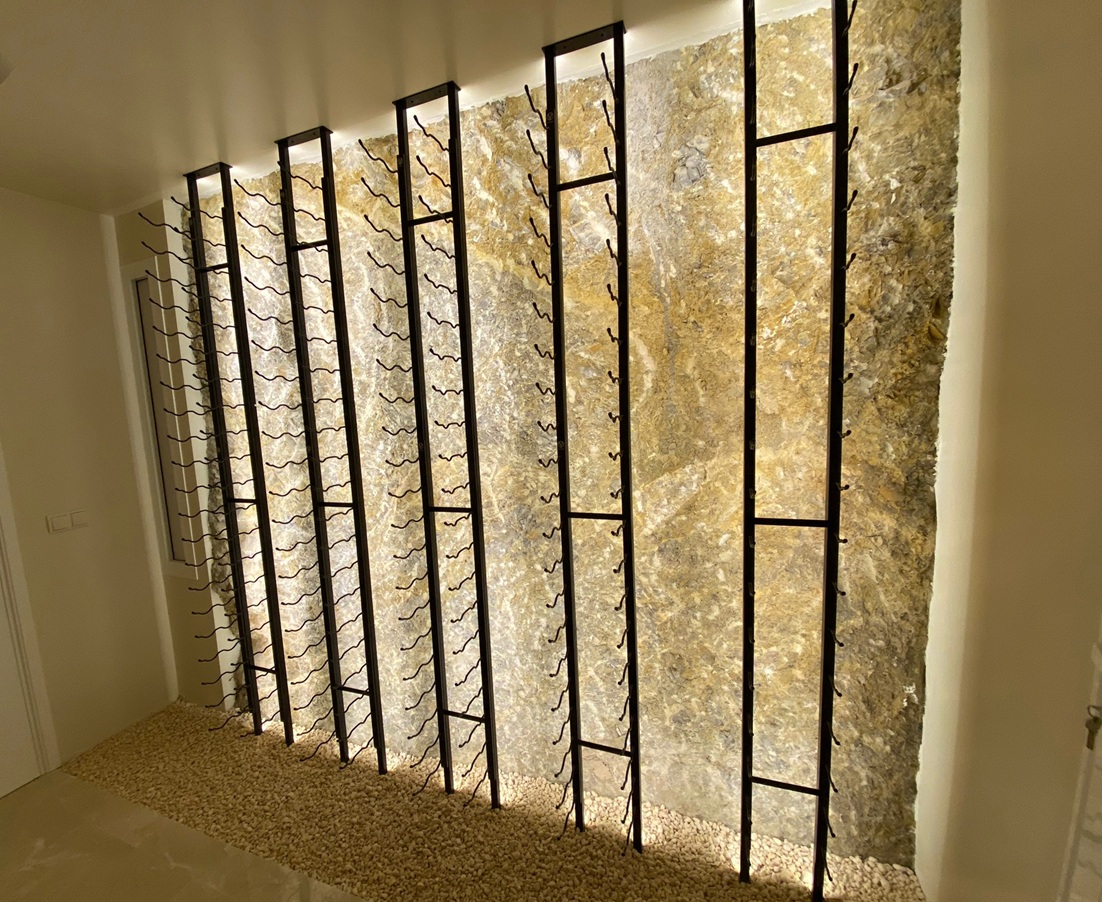 Muro de vino de piedra retroiluminado con soportes negros de pared para botellas de vino.