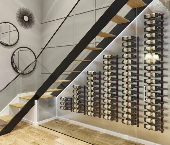 Instalación bajo escalera con soportes de pared para botellas de vino que aprovecha el espacio y crea un muro de vino moderno.