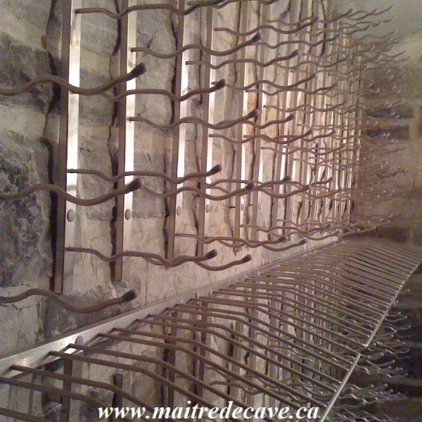 Soportes metálicos de pared para botellas de vino instalados sobre una pared de piedra para crear un almacenamiento arquitectónico.